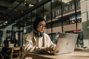 A focused woman wearing a headscarf works on her laptop in a stylish urban cafe.