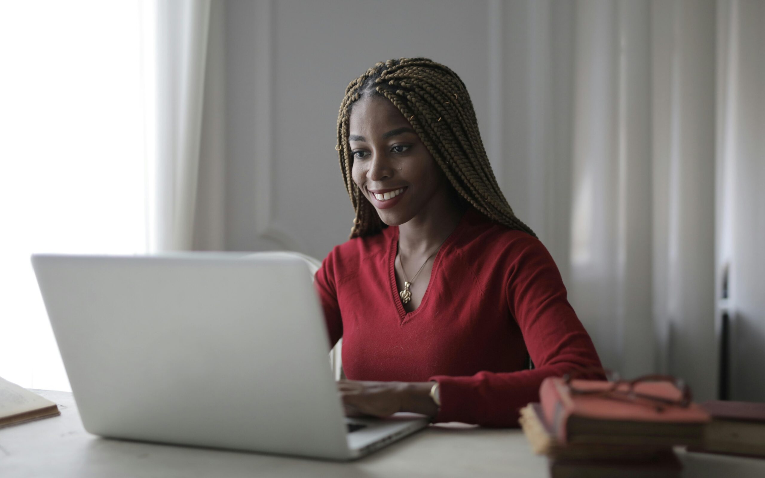 A joyful woman in a red top working on a laptop at home, embodying remote work happiness.