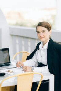 Young woman in a black blazer, working outdoors on a laptop, embodying professionalism.