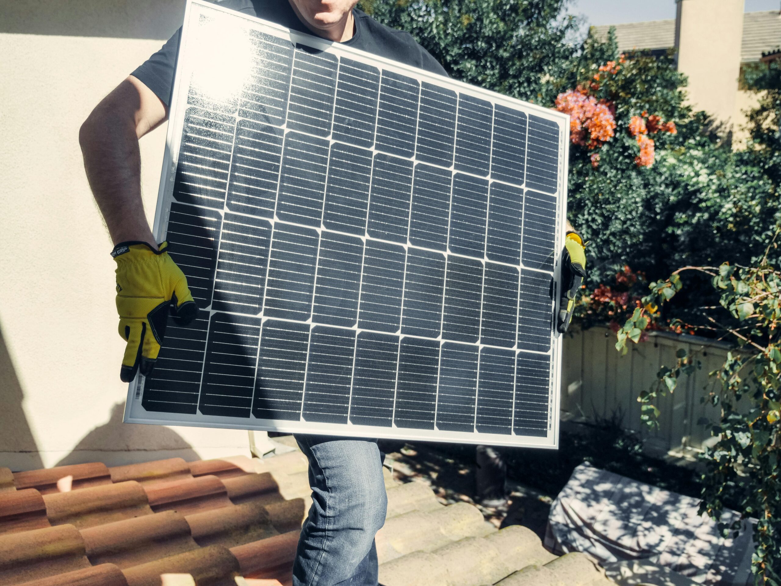 Technician carrying solar panel on rooftop. Clean energy installation outdoors.