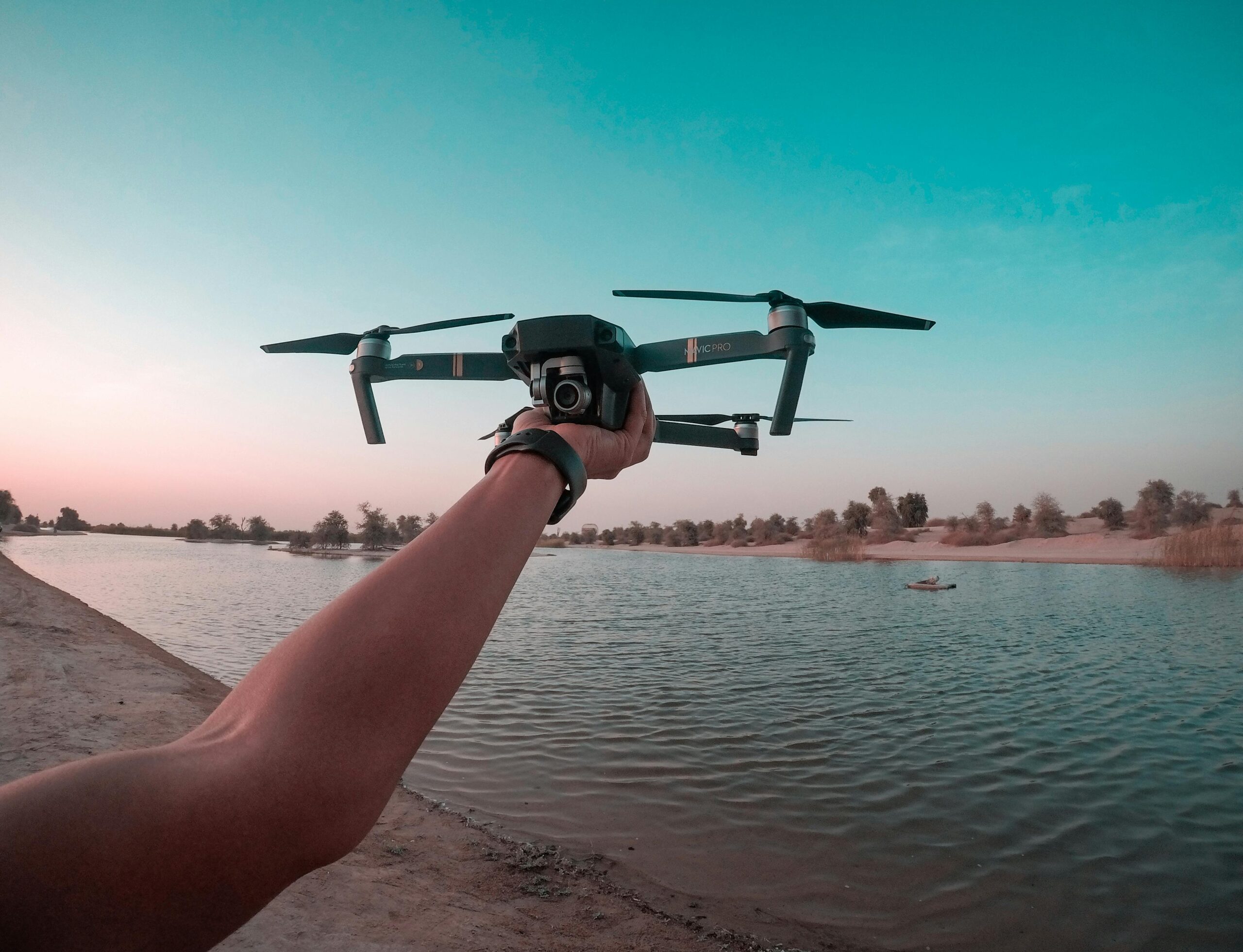 A person holds a drone over a lake in the Dubai desert, showcasing a scenic aerial view.