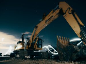 A powerful excavator at a construction site under the night sky, with workers around.