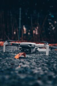 A close-up shot of a drone on a concrete surface surrounded by autumn leaves.