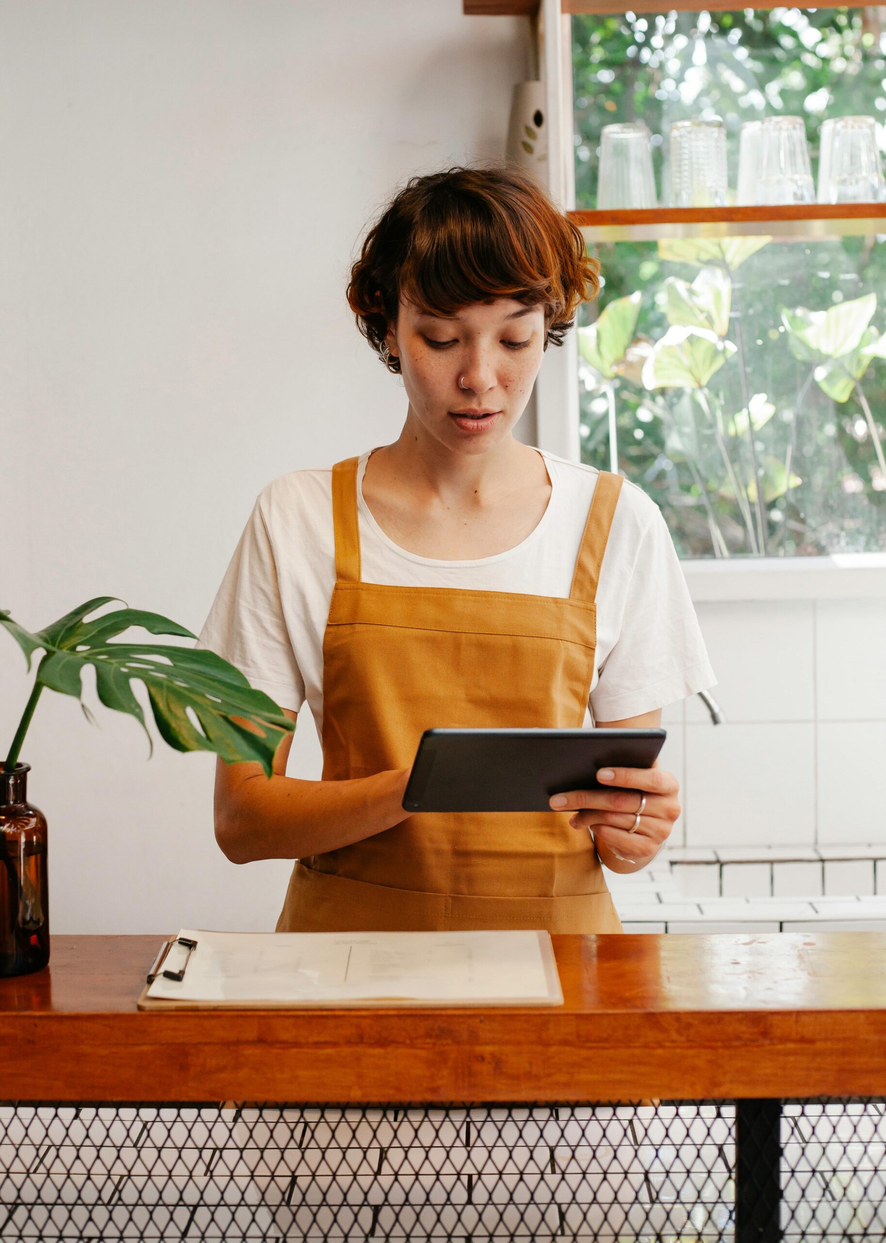 Young attentive female worker in apron surfing internet on tablet while working in cafeteria