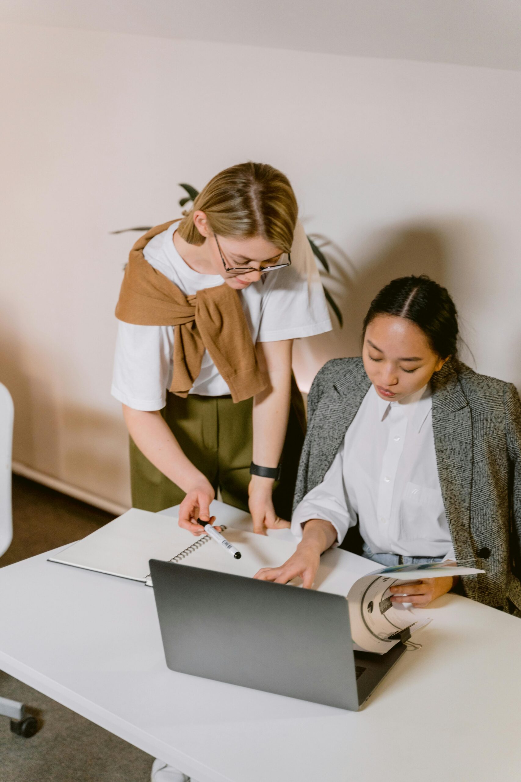 Two diverse colleagues brainstorm over a laptop in a modern office setting.