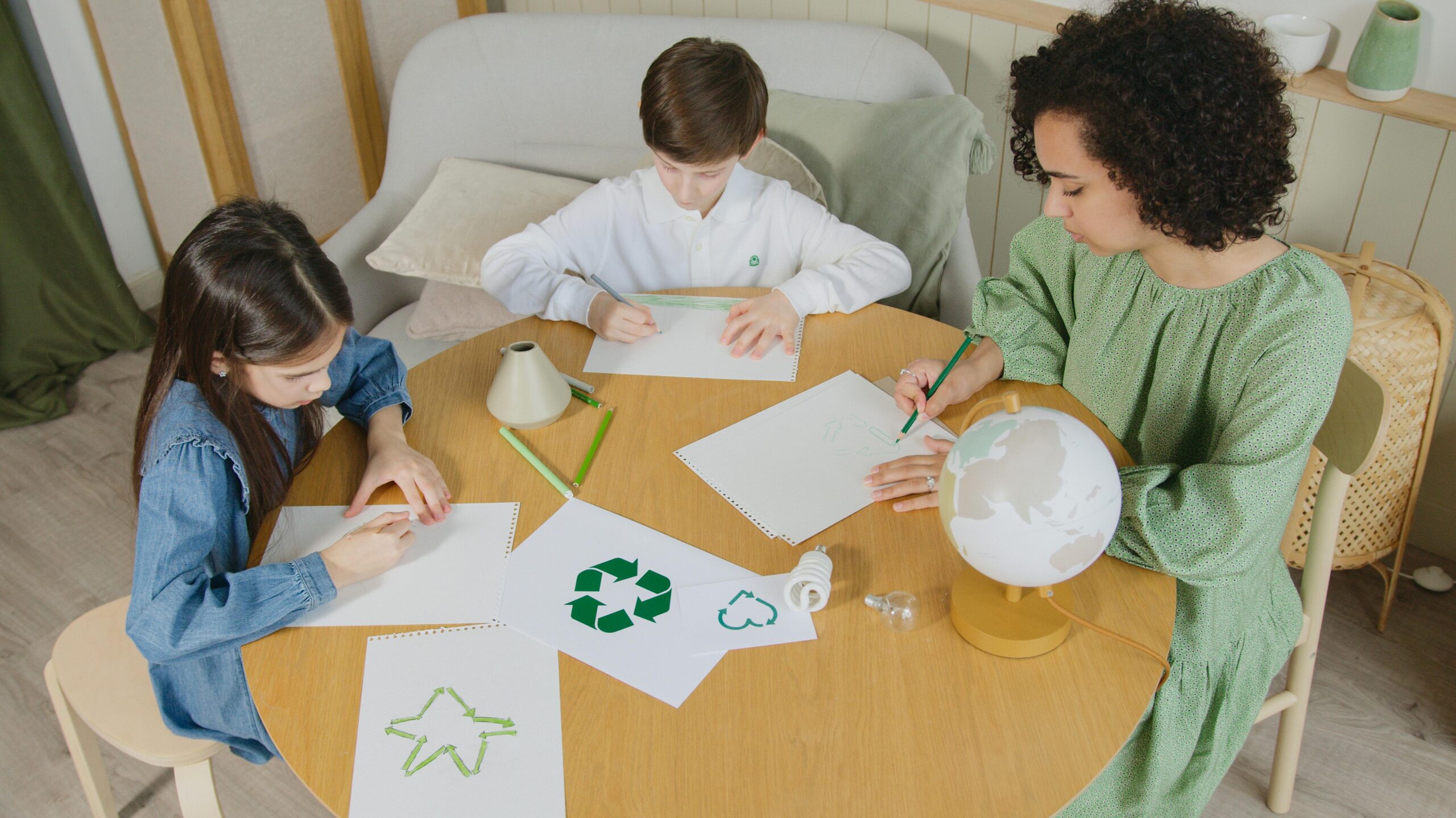 Children drawing eco-friendly symbols with a teacher in an indoor classroom setting.