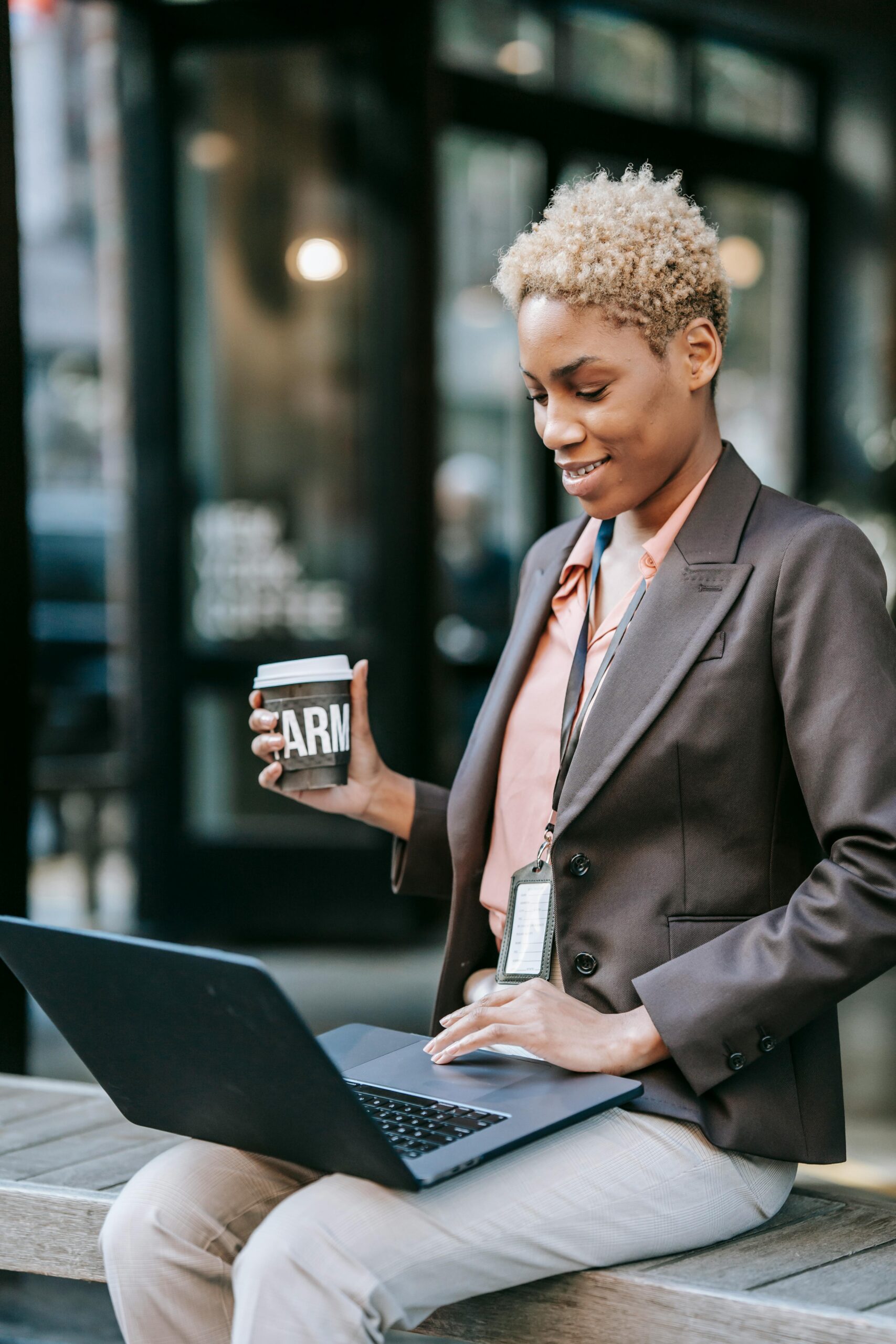 Businesswoman sitting outdoors with a laptop, enjoying coffee break.