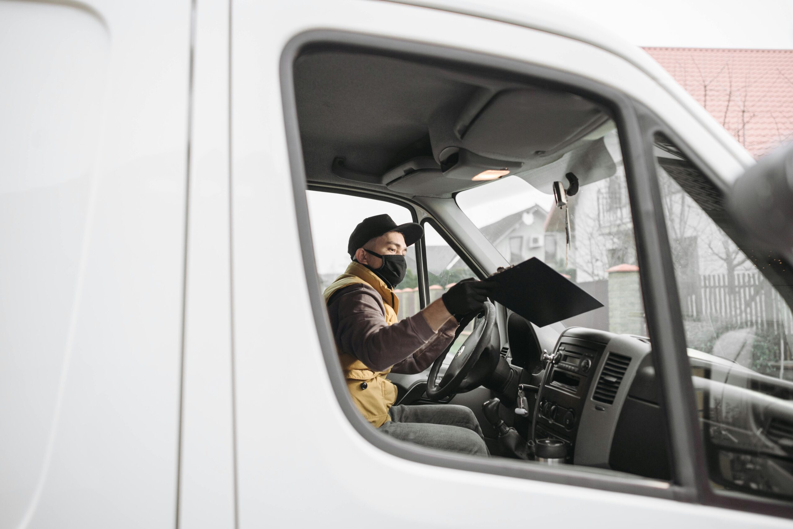 Masked delivery person inside a van holding a clipboard, illustrating modern delivery service.