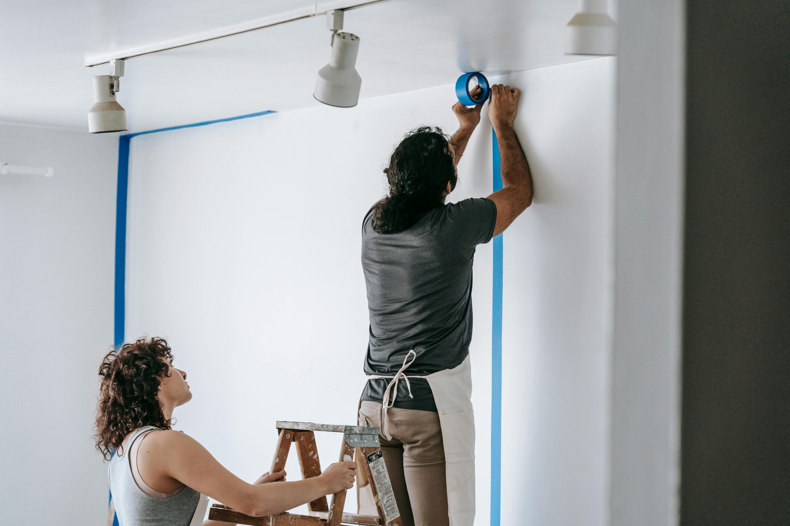 A man and woman working together on home renovation, applying painter's tape.