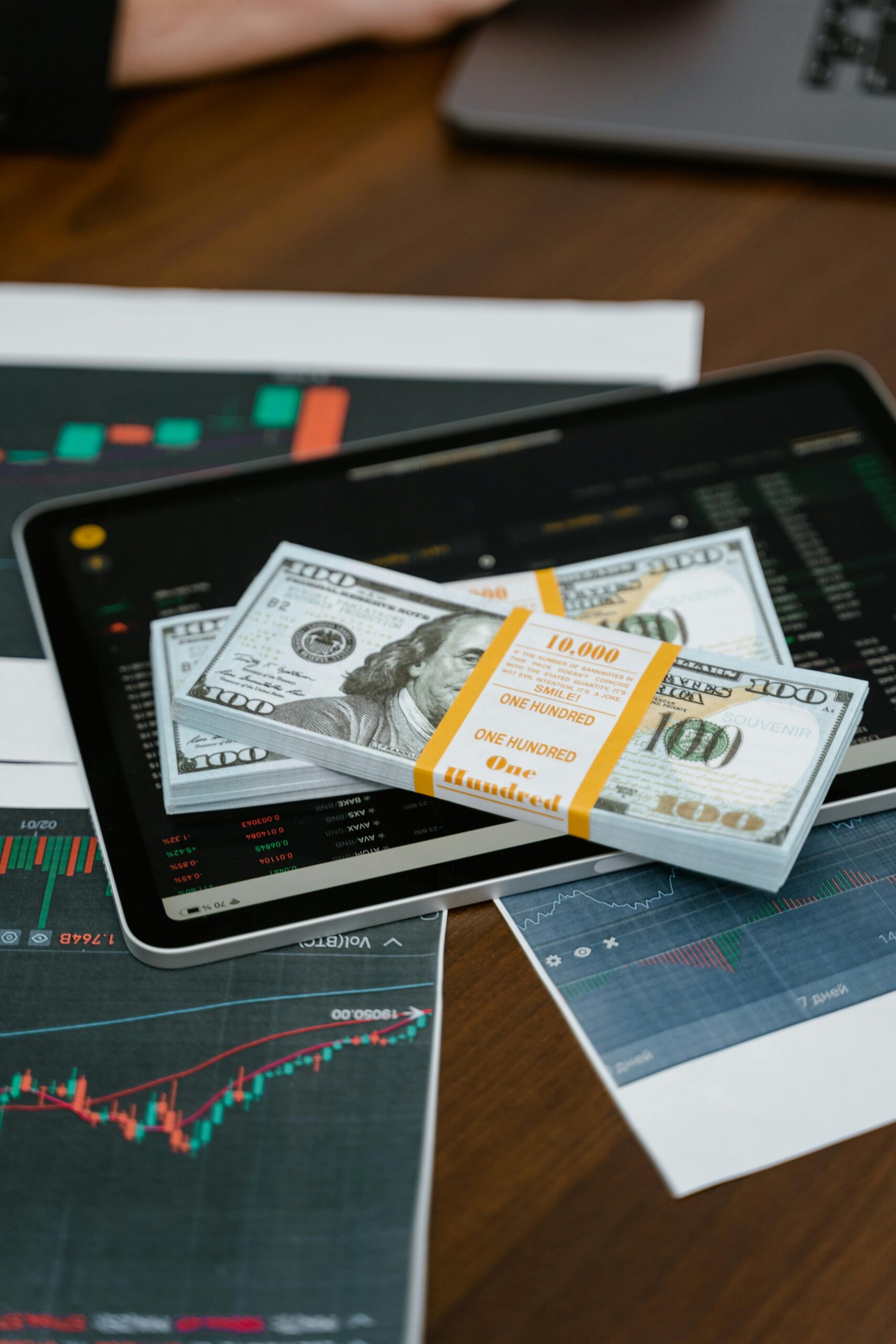 Stack of $100 bills placed on a tablet with financial graphs, symbolizing digital finance.