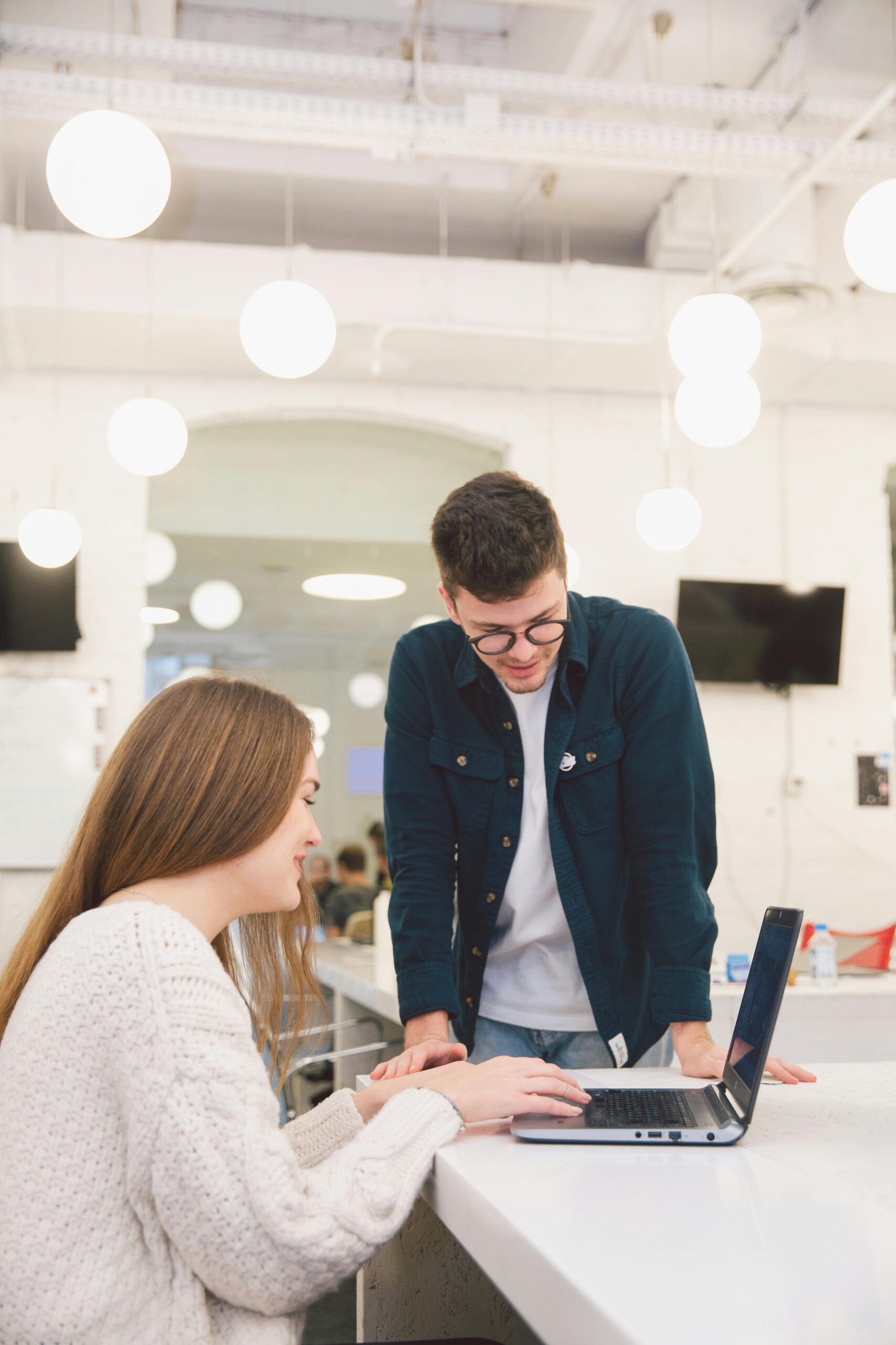 Two young adults collaborating over a laptop in a modern, bright office setting.