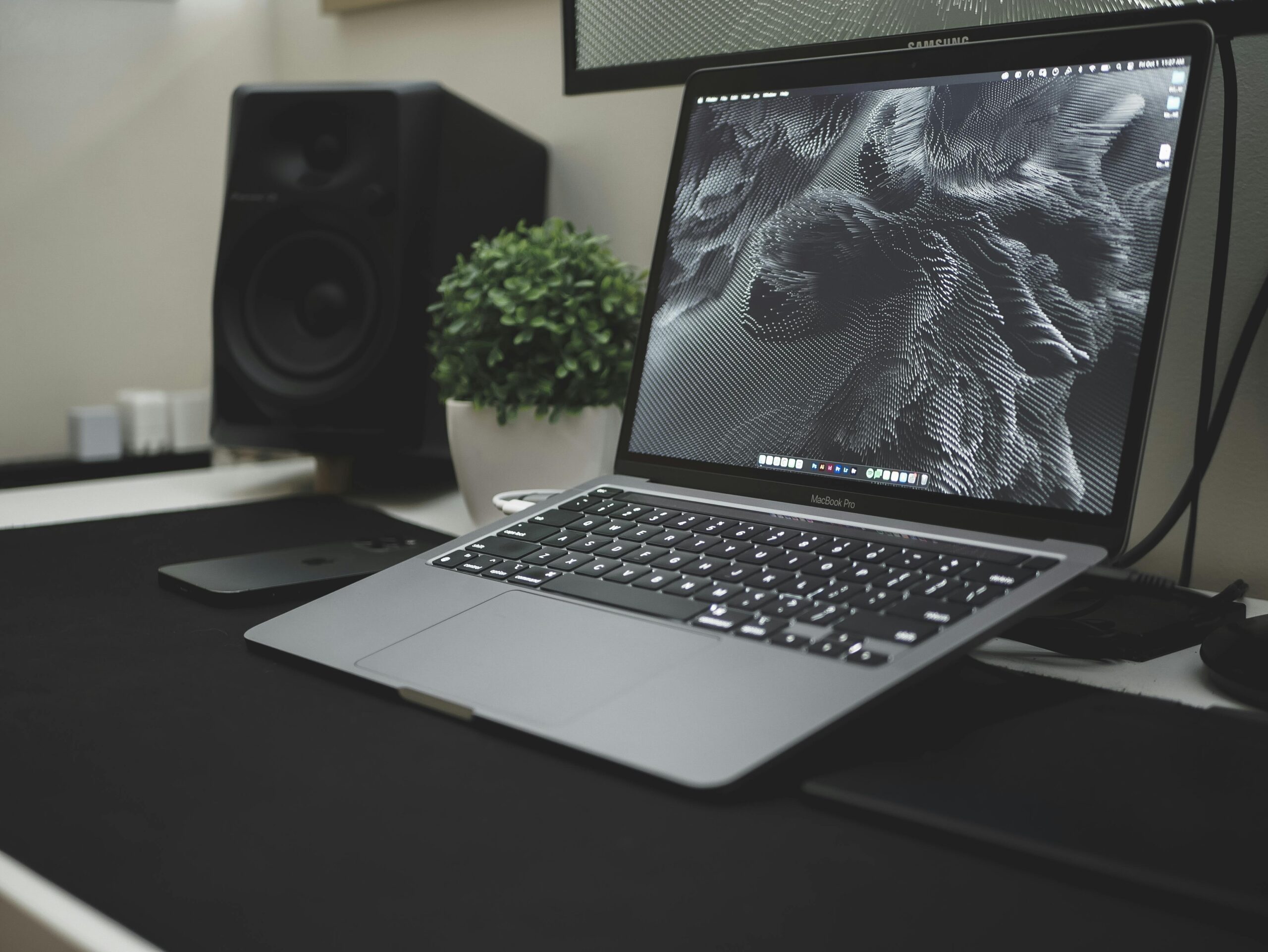 A sleek workspace featuring a laptop, speaker, and plant, showcasing modern technology and design.